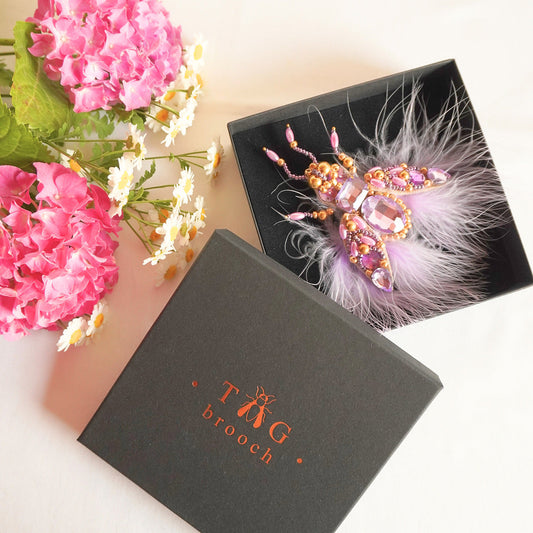 Handmade beaded fly brooch with feathers and gemstones on a black box with TGbrooch branding