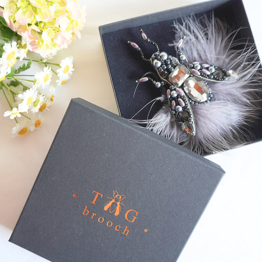 Handmade beaded fly brooch with grey feathers and black and silver beads in a TGbrooch box